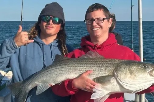 Two people on a boat holding a large fish, with one making a thumbs-up gesture.