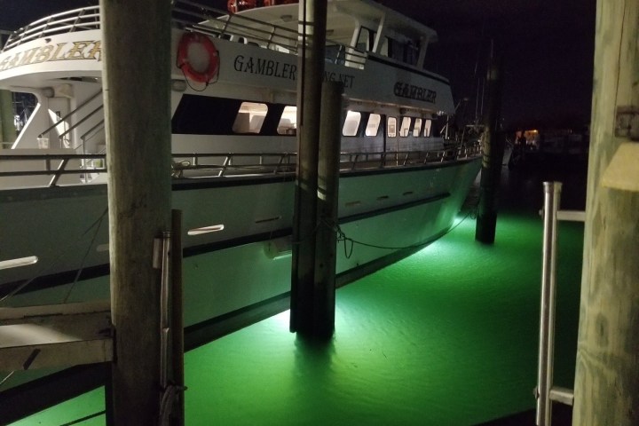 Boat docked at night with green underwater lights illuminating water.